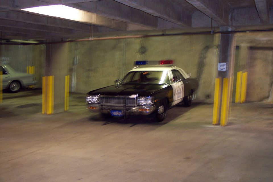 Black and white police car with light bar, parked in a garage. License plate is visible