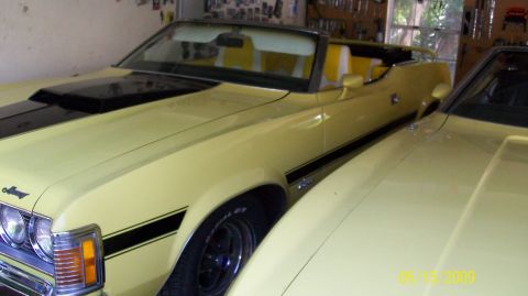 1973 Mercury Cougar - This 1973 Mercury Cougar convertible features a distinctive black stripe and hood scoop, parked next to another yellow vehicle.
