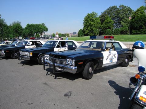 1991 Ford LTD Crown Victoria - black-and-white highway patrol Dodge with a brush guard and roof lightbar is parked outdoors among other vintage police cars and a motorcyc…