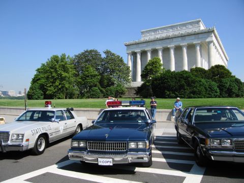 1991 Ford LTD Crown Victoria - Several patrol cars, one labeled COPS and another STATE POLICE, are parked on pavement in front of the columned Lincoln Memorial.