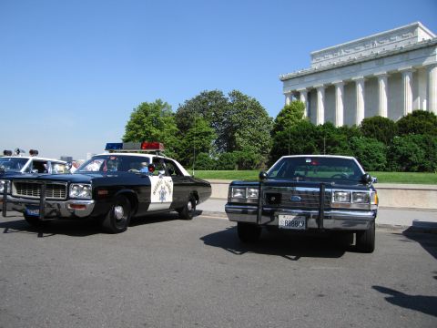 1991 Ford LTD Crown Victoria - vintage black-and-white police cruiser and a black modern Ford sedan parked on a roadway in front of the Lincoln Memorial.