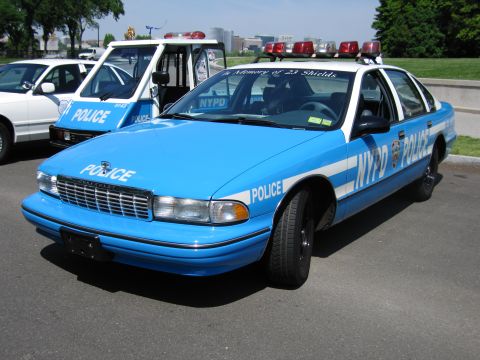 1991 Ford LTD Crown Victoria - light-blue NYPD Chevrolet Caprice patrol sedan with white stripe and Police markings, parked on a paved lot.