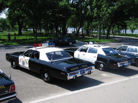 1991 Ford LTD Crown Victoria - black-and-white sedan marked Highway Patrol with CHP star, parked among other vintage police cruisers under trees.