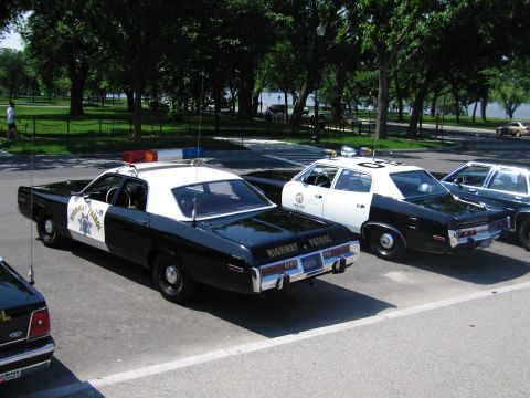 1991 Ford LTD Crown Victoria - Rear three-quarter view of a black-and-white Highway Patrol sedan parked beside white and black police cars near water.