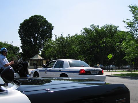 1991 Ford LTD Crown Victoria - white and blue sedan marked United States Park Police on a roadway, viewed over the roof of a foreground car with an officer at left.