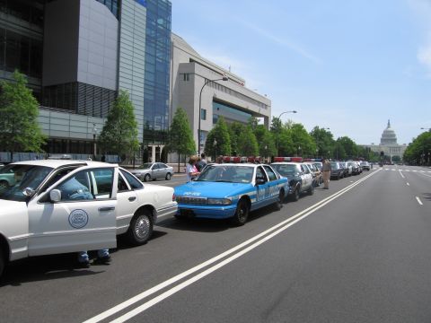 1991 Ford LTD Crown Victoria - White and blue police patrol sedans parked along a city street with the US Capitol dome visible in the distance.