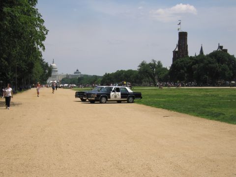 1991 Ford LTD Crown Victoria - black-and-white sedan police car is parked on a gravel path on the National Mall with the U.S. Capitol dome visible in the distance.