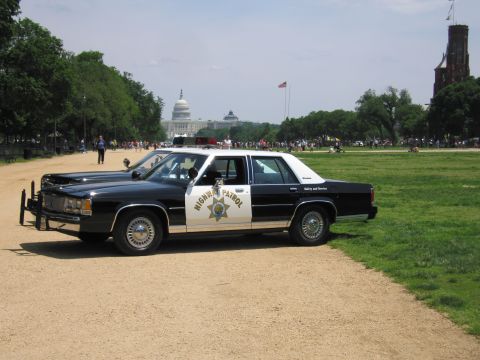 1991 Ford LTD Crown Victoria - black-and-white Ford Highway Patrol sedan with a star door shield is parked on the grass of the National Mall with the Capitol in the backg…