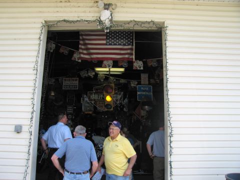 1991 Ford LTD Crown Victoria - Several men stand in the open doorway of a cluttered garage decorated with a U.S. flag, a traffic light, and assorted signs.
