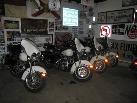 1991 Ford LTD Crown Victoria - row of white police motorcycles sits parked inside a garage whose walls are covered with flags, signs, and memorabilia.
