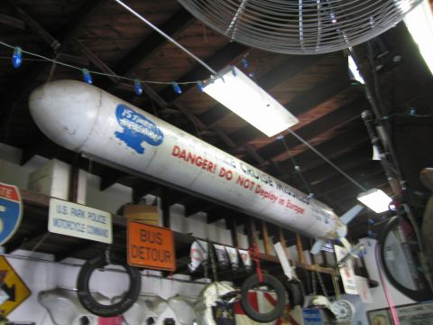 1991 Ford LTD Crown Victoria - large white missile-shaped object marked DANGER! DO NOT Deploy in Europe hangs from the rafters of a sign-covered garage.