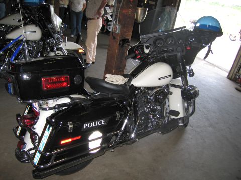 1991 Ford LTD Crown Victoria - black-and-white Harley-Davidson police touring motorcycle marked POLICE on its saddlebag, parked inside a garage with a blue helmet nearby.
