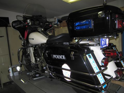 1991 Ford LTD Crown Victoria - Rear-left view of a black-and-white police touring motorcycle marked POLICE, raised on a lift inside a workshop with lockers behind.