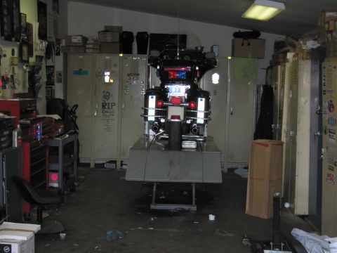 1991 Ford LTD Crown Victoria - Rear view of a police touring motorcycle raised on a lift in a cluttered, dimly lit garage with metal lockers and tool chests.