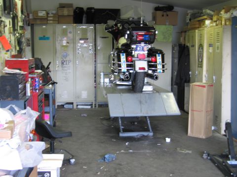 1991 Ford LTD Crown Victoria - police touring motorcycle raised high on a lift in a cluttered workshop with beige lockers and tool storage.