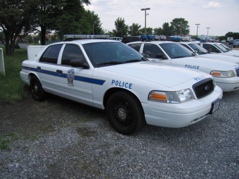 1991 Ford LTD Crown Victoria - Front-right view of a white Ford Crown Victoria police sedan marked POLICE, parked with similar cruisers on a gravel lot.