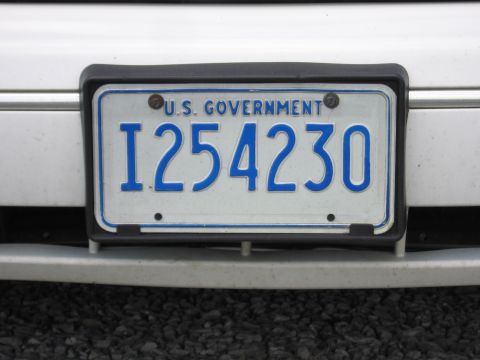 1991 Ford LTD Crown Victoria - blue-on-white U.S. Government license plate reading I254230 mounted in a black frame on a white vehicle bumper.