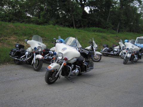 1991 Ford LTD Crown Victoria - group of white police touring motorcycles with windshields parked on pavement beside a grassy bank, a cruiser in the background.