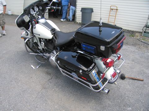 1991 Ford LTD Crown Victoria - Rear-left view of a black-and-white police touring motorcycle marked POLICE with a top box and antenna, parked outdoors by a building.