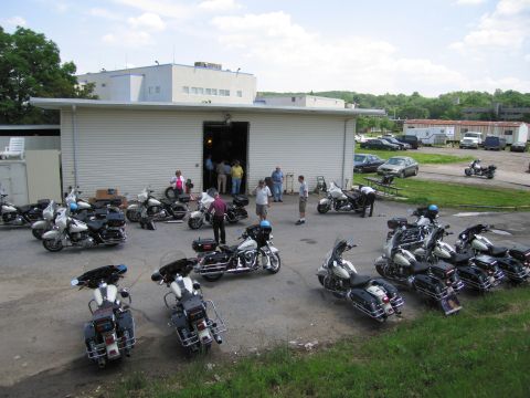 1991 Ford LTD Crown Victoria - Many police touring motorcycles arranged in a wide circle on pavement outside a white industrial building, people gathered at the door.