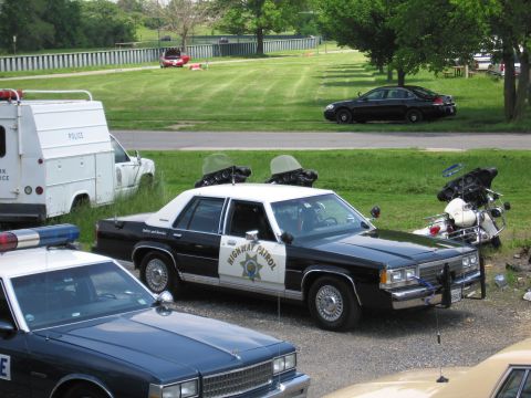 1991 Ford LTD Crown Victoria - black-and-white HIGHWAY PATROL sedan parked on grass with two police motorcycles behind it and other cruisers in front.