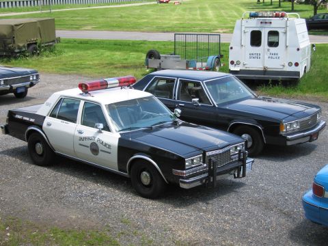 1991 Ford LTD Crown Victoria - black-and-white Jaffrey Police sedan with a red roof lightbar sits on gravel next to a black sedan and a United States Park Police utility…