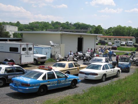 1991 Ford LTD Crown Victoria - gathering of police vehicles, including a blue NYPD sedan, a white cruiser, a prisoner-transport trailer and motorcycles, fills a lot by a…