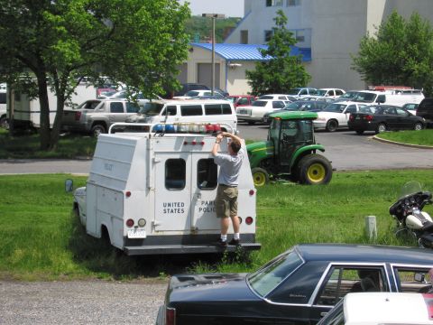 1991 Ford LTD Crown Victoria - man stands on the rear bumper of a white United States Park Police utility truck, reaching up to work on its roof lightbar.