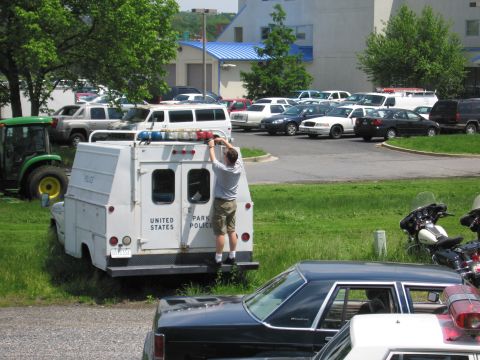 1991 Ford LTD Crown Victoria - man perched on a white United States Park Police utility truck services its roof lights, with a packed parking lot and a green tractor behi…