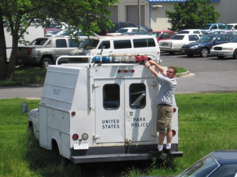 1991 Ford LTD Crown Victoria - man stands on the rear platform of a white United States Park Police utility truck, adjusting the emergency lights on its roof rack.