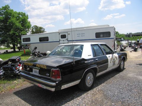 1991 Ford LTD Crown Victoria - rear of a black-and-white Highway Patrol-marked Ford sedan parked beside police motorcycles and a United States Park Police trailer.