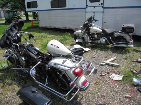 1991 Ford LTD Crown Victoria - Two white police Harley-Davidson touring motorcycles lie tipped over on the gravel beside a Park Police trailer, with debris scattered arou…