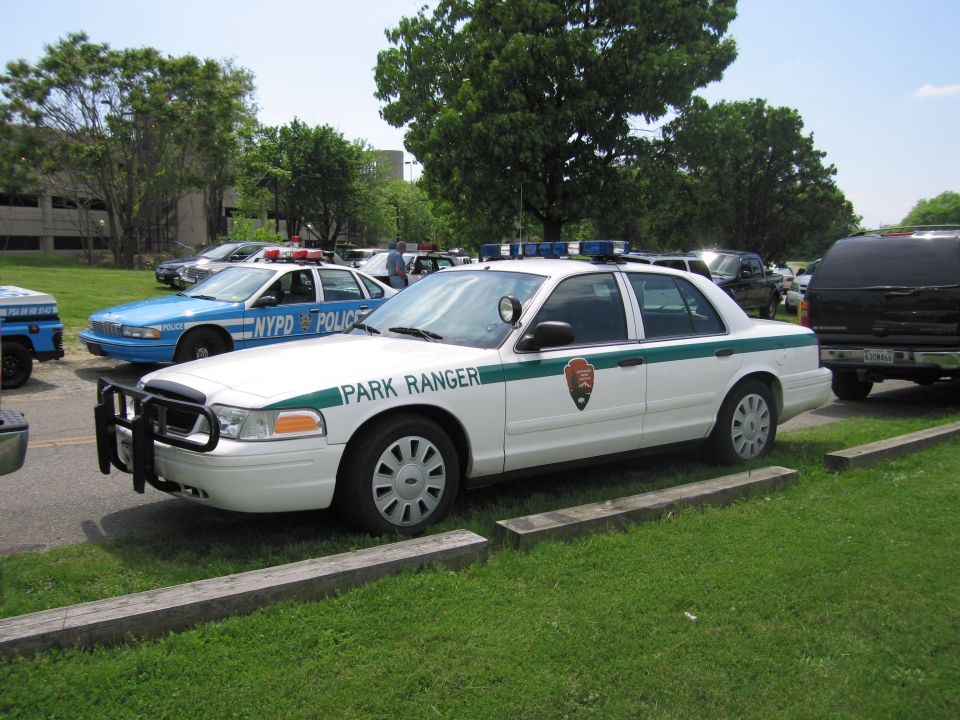 White and green Park Ranger Ford Crown Victoria with NPS arrowhead parked on grass near a blue NYPD cruiser
