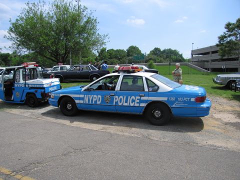1991 Ford LTD Crown Victoria - blue NYPD Chevrolet Caprice cruiser marked 1350 103 PCT parks beside an NYPD tow truck, with other classic cars behind.