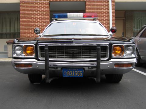 1991 Ford LTD Crown Victoria - front of a black-and-white police car with a DODGE grille badge shows twin spotlights, a chrome push bar and a roof lightbar.