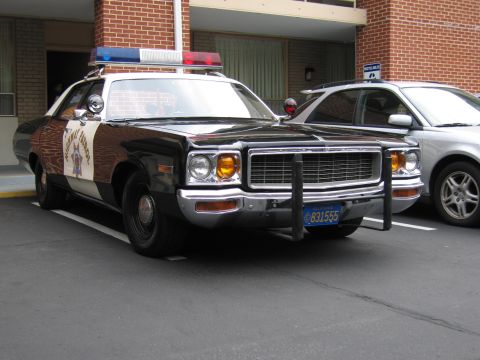 1991 Ford LTD Crown Victoria - black-and-white California Highway Patrol-marked Dodge sedan with a push bar and roof lights parks at a brick building next to a silver car.