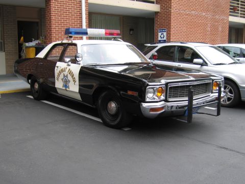 1991 Ford LTD Crown Victoria - black-and-white California Highway Patrol Dodge sedan with a gold star emblem and chrome push bar sits angled in a brick motel lot.