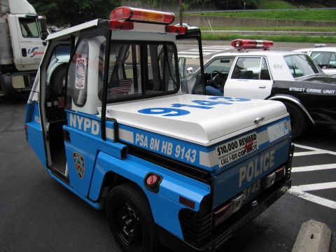 1991 Ford LTD Crown Victoria - blue and white NYPD three-wheeled police scooter numbered 9143 sits in a parking lot beside marked patrol cars.