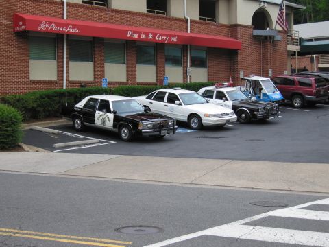 1991 Ford LTD Crown Victoria - Several police vehicles, including a black and white Highway Patrol sedan, parked along a brick restaurant facade.