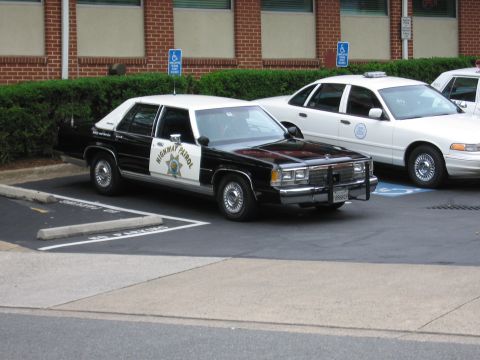 1991 Ford LTD Crown Victoria - black and white Highway Patrol Ford sedan with a push bumper parked beside white marked patrol cars.