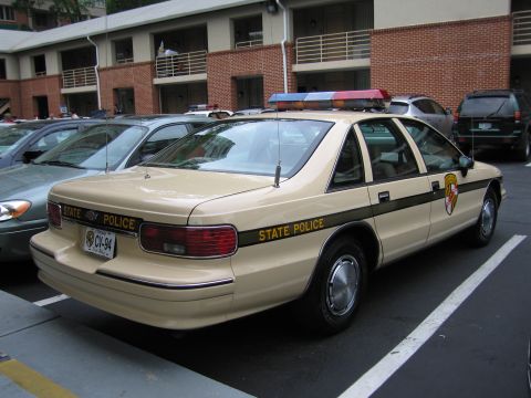 1991 Ford LTD Crown Victoria - tan Chevrolet Caprice marked State Police with Maryland plate CV-94 parked in a motel lot.