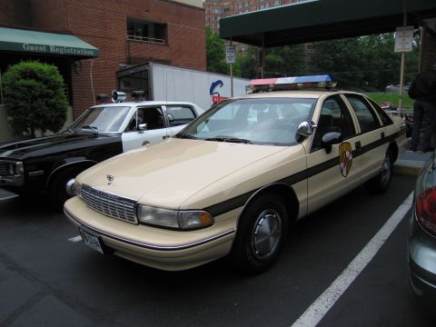 1991 Ford LTD Crown Victoria - Front three-quarter view of a tan Chevrolet Caprice marked State Police parked at a hotel guest registration entrance.