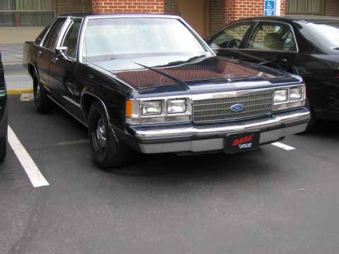 1991 Ford LTD Crown Victoria - black Ford LTD Crown Victoria sedan bearing a red DARE decal on the front bumper parked in a lot.