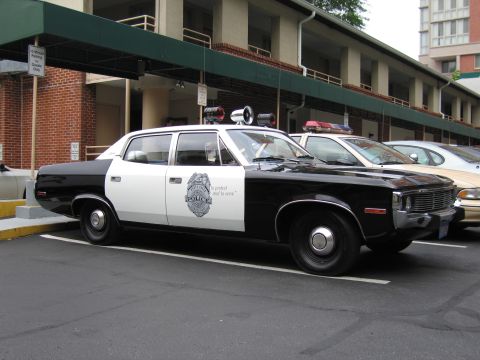 1991 Ford LTD Crown Victoria - Side view of a black and white AMC police sedan with a door badge and roof lights parked at a motel.