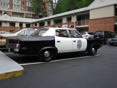 1991 Ford LTD Crown Victoria - Rear quarter view of a black and white AMC police sedan with a door badge parked among other cars at a motel.