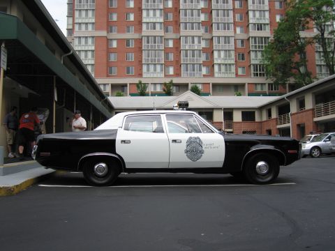 1991 Ford LTD Crown Victoria - Side profile of a black and white police sedan with a door badge parked in front of a brick high-rise building.