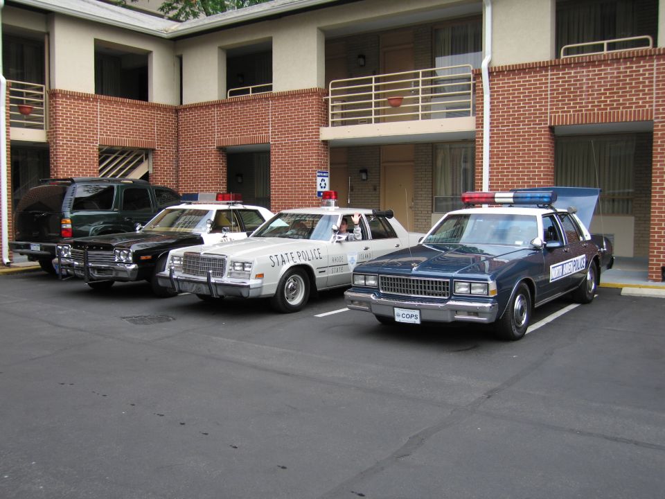 Three vintage police cars including a State Police sedan parked in a motel lot