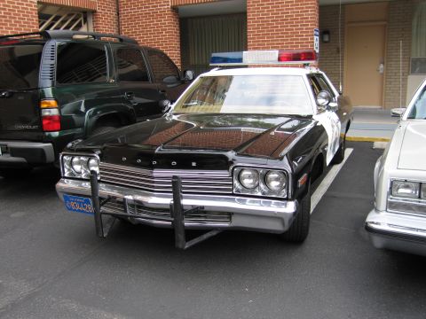 1991 Ford LTD Crown Victoria - black and white Dodge police sedan with a push bumper and DODGE grille lettering parked beside an SUV at a motel.