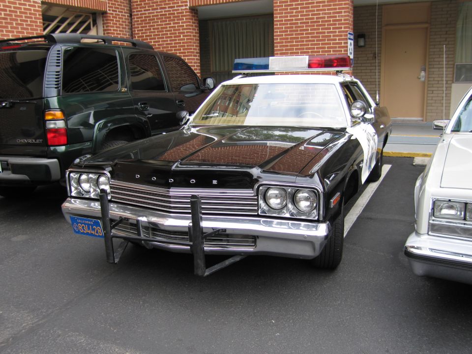 Black and white Dodge police sedan with push bumper and DODGE grille lettering parked at a motel