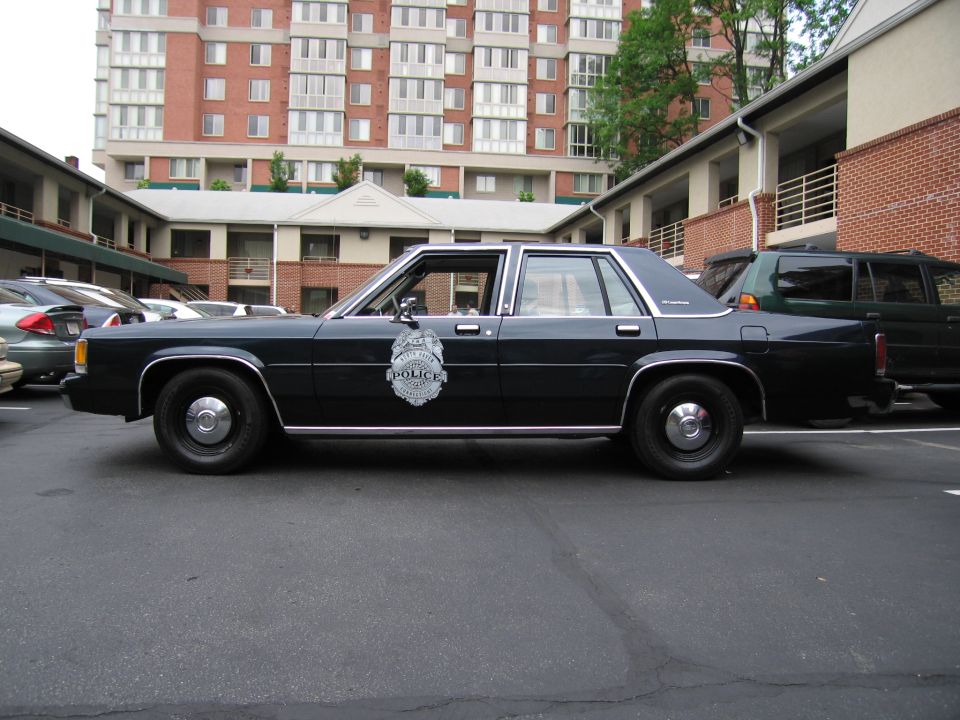 Profile of dark blue Ford LTD Crown Victoria police sedan in parking lot by apartment buildings